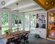 a dining room table with chairs and bookshelves in front of glass doors leading to an outside deck