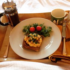 a white plate topped with toast and vegetables next to a cup of coffee on top of a wooden tray