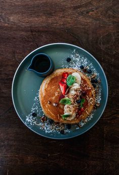 a pancake with fruit, nuts and powdered sugar sits on a blue plate