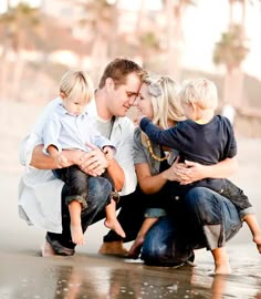 a man, woman and two children are sitting on the beach with their arms around each other