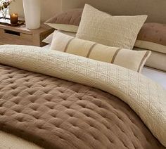 a bed with brown and white comforters on top of it next to a window