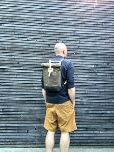 a man standing in front of a building with a back pack on his back, looking down at the ground