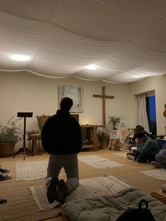 people are sitting on the floor in a room with white walls and ceilings, while one person is standing