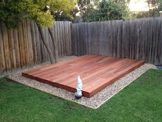 a wooden deck in the middle of a yard with grass around it and a fence behind it