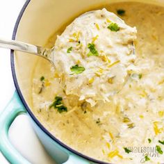 a ladle full of creamed chicken soup with parsley on the spoon in a blue pot