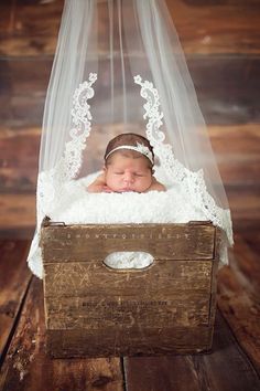 a baby is sleeping in a wooden box with a white veil over it's head