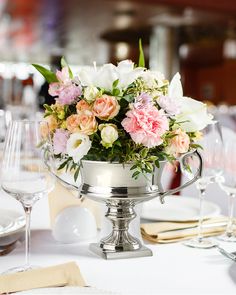 a silver vase filled with lots of flowers on top of a white table cloth covered table