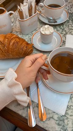 a person is sitting at a table with coffee and croissants