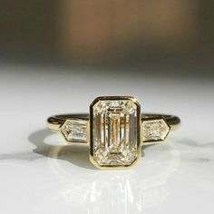 an emerald cut diamond ring with three baguets on the band and side stones