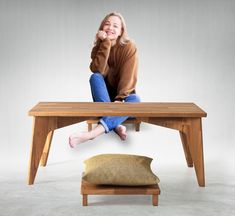 a woman sitting on top of a wooden table next to a brown pillow with her legs crossed