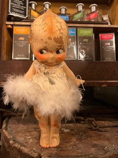 an old fashioned doll sitting on top of a wooden table in front of a shelf