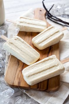 three popsicles sitting on top of a wooden cutting board next to a glass of milk