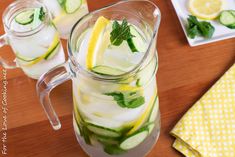 a pitcher filled with cucumber and lemonade on top of a wooden table