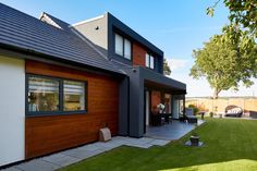 a modern house with wood siding and black shingles on the roof, along with green grass