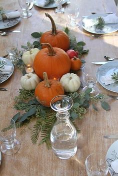 a table topped with lots of pumpkins and greenery on top of a wooden table