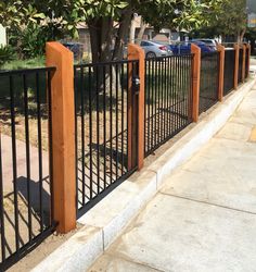 an iron fence with wood posts and gate on the side of a sidewalk next to a tree