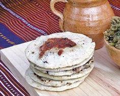 a stack of tortillas sitting on top of a wooden cutting board next to a pot