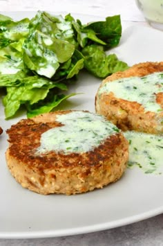 two crab cakes on a white plate with lettuce and sauce next to it