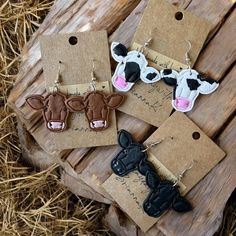 four pairs of cow earrings with tags attached to them on top of some wood planks