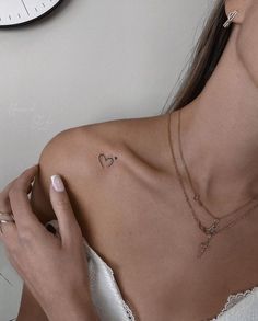 a woman with a heart tattoo on her left shoulder, next to a wall clock