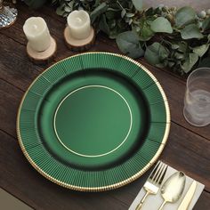 a green plate with gold trim sits on a wooden table next to silverware and candles