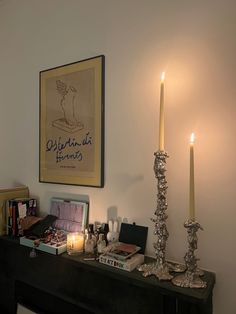 a couple of candles sitting on top of a wooden table next to a painting and some books