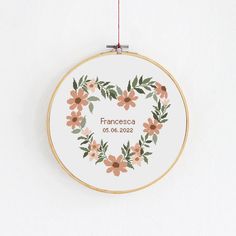 a cross stitch heart with flowers and leaves is hanging on a wall ornament