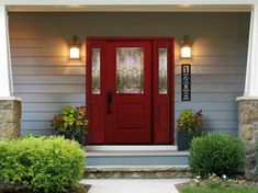 a red front door on a gray house with white columns and pillars, surrounded by greenery