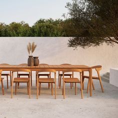 a wooden table with six chairs and a vase on it next to a white wall