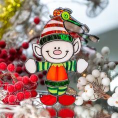 a glass ornament with a christmas elf on it's head, surrounded by red berries