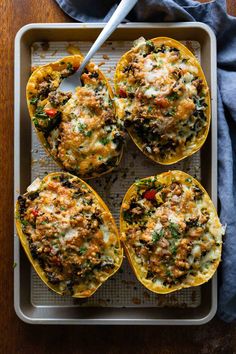 four stuffed bell peppers on a baking sheet with a spoon in it and a blue napkin next to them