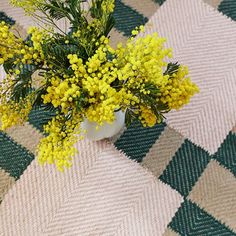 a white vase filled with yellow flowers on top of a checkered tablecloth covered floor