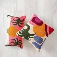 two colorful pillows sitting on top of a white bed next to each other, one with an octopus design