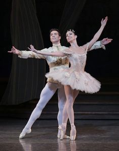 two ballerinas in white tutus and gold headdress, one holding the other's leg