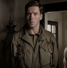 a man standing in front of a mirror wearing an army jacket and looking at the camera