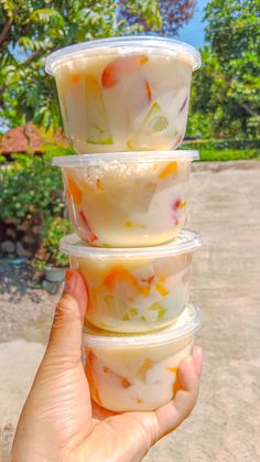 a person holding three plastic containers with food in it's palm hand and trees in the background