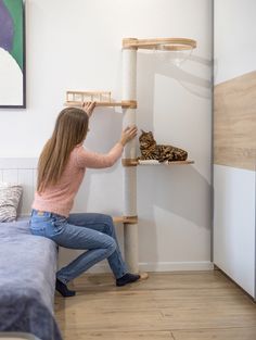 a woman is reaching up to reach the top of a cat scratch tree in her living room