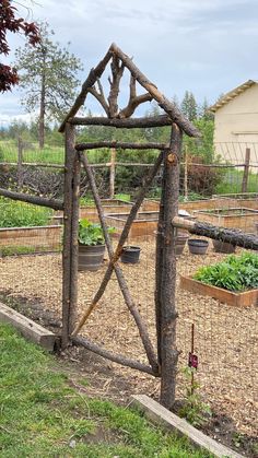 a wooden gate made out of branches in the middle of a garden filled with plants