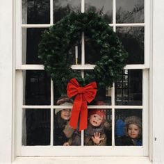 two children looking out the window with a christmas wreath