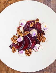 a white plate topped with beets and walnuts on top of a wooden table