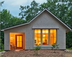 a small house is lit up at night in the woods with trees and shrubs surrounding it