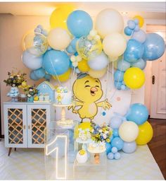 a table topped with balloons and cake next to a white table cloth covered wall filled with blue, yellow and white balloons