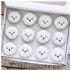 twelve cupcakes with white frosting in a box on top of a wooden table