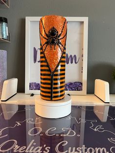 an orange and black striped vase sitting on top of a glass table next to a white frame