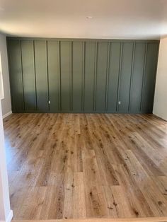 an empty room with wood flooring and green painted wall behind the door to another room