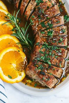 a plate with meat, oranges and gravy next to some sliced lemons