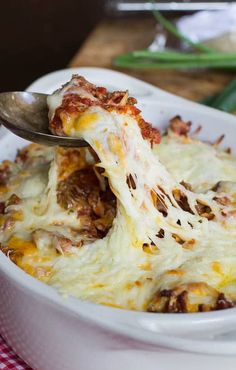 a white bowl filled with lasagna covered in cheese and meat, topped with a spoon