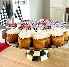 cupcakes with white frosting and race cars on them sitting on a cake plate