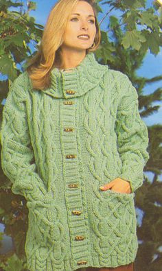 a woman wearing a green cabled sweater and brown pants with trees in the background