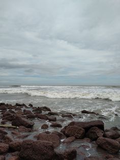 rocks on the beach with waves coming in from the ocean and cloudy sky above them